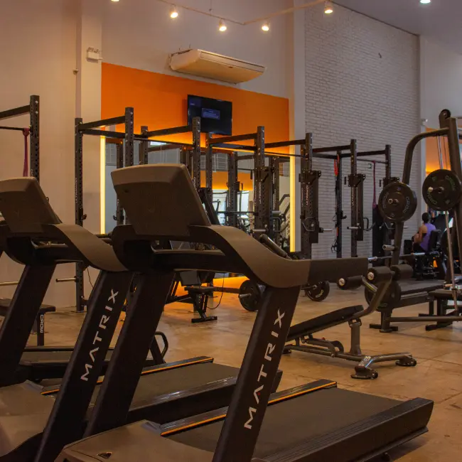 Interior de uma academia moderna com esteiras Matrix e power racks, ideal para personal training e treinos em grupo.