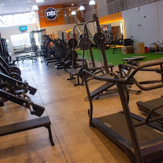 Academia moderna e espaçosa com equipamentos de musculação, power racks, pesos livres e esteiras para personal training e treino em grupo.