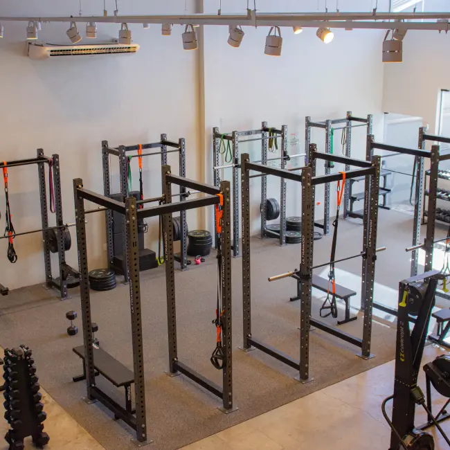 Academia moderna com power racks, halteres, barras e equipamentos de cardio para personal training e treinamento em grupo.