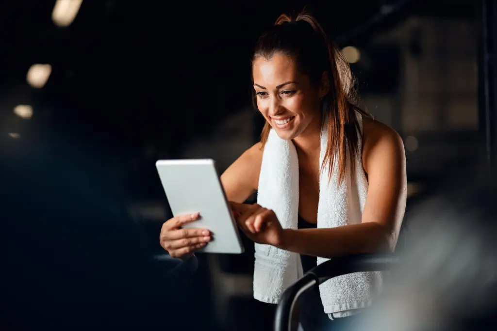 Mulher sorridente no treino com tablet, otimizando seu personal training na academia com tecnologia e acompanhamento.