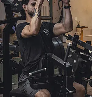 Homem focado em treino de força de braços em máquina de bíceps, personal training personalizado para resultados eficazes.