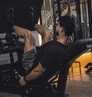 Homem fazendo leg press em academia, treino de pernas personalizado, fortalecimento muscular com personal trainer.