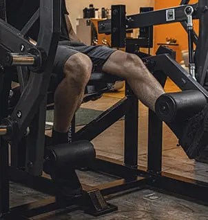 Homem realizando extensão de pernas em máquina de academia, fortalecendo quadríceps. Treino personalizado para pernas.